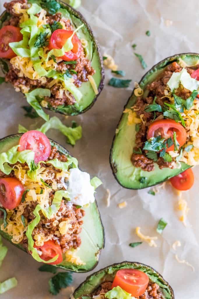 Overhead picture of halved avocados filled with taco meat, tomato, lettuce, cheese and sour cream.